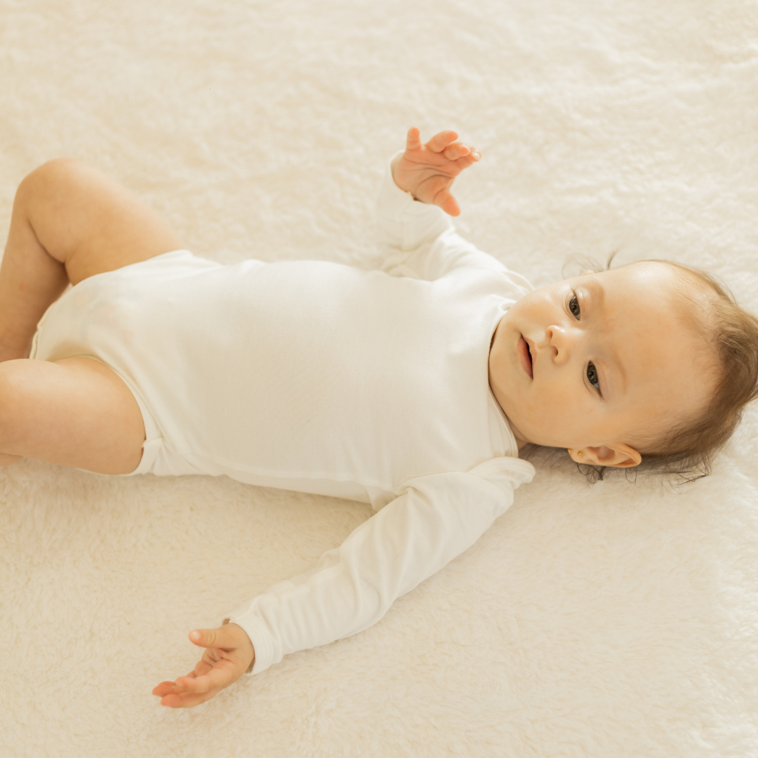 Recém-nascido vestindo body de viscose sustentável branco deitado em superfície clara com luz natural